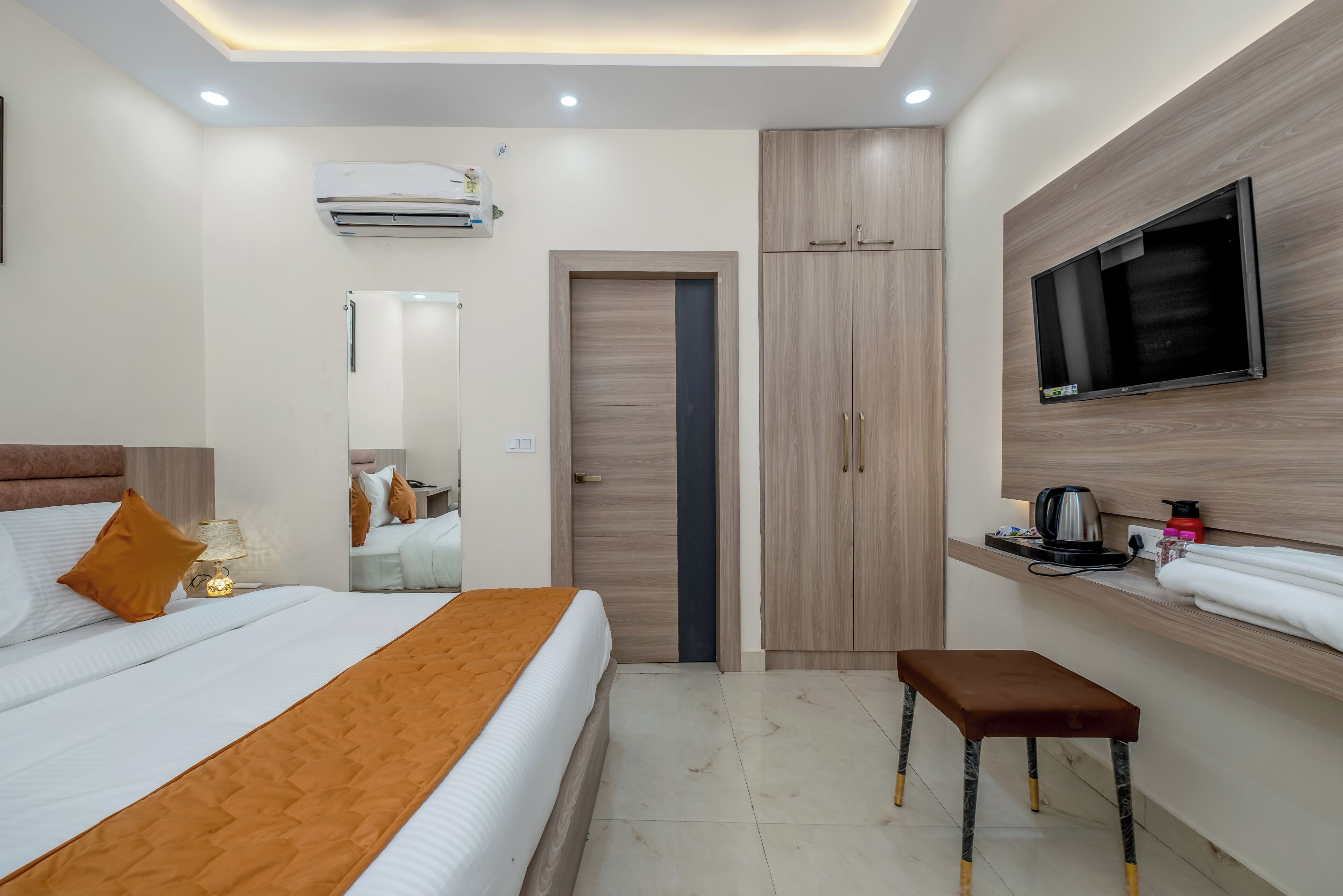 A modern hotel room with a bed, a TV mounted on the wall, a wardrobe, and a small table with a kettle.