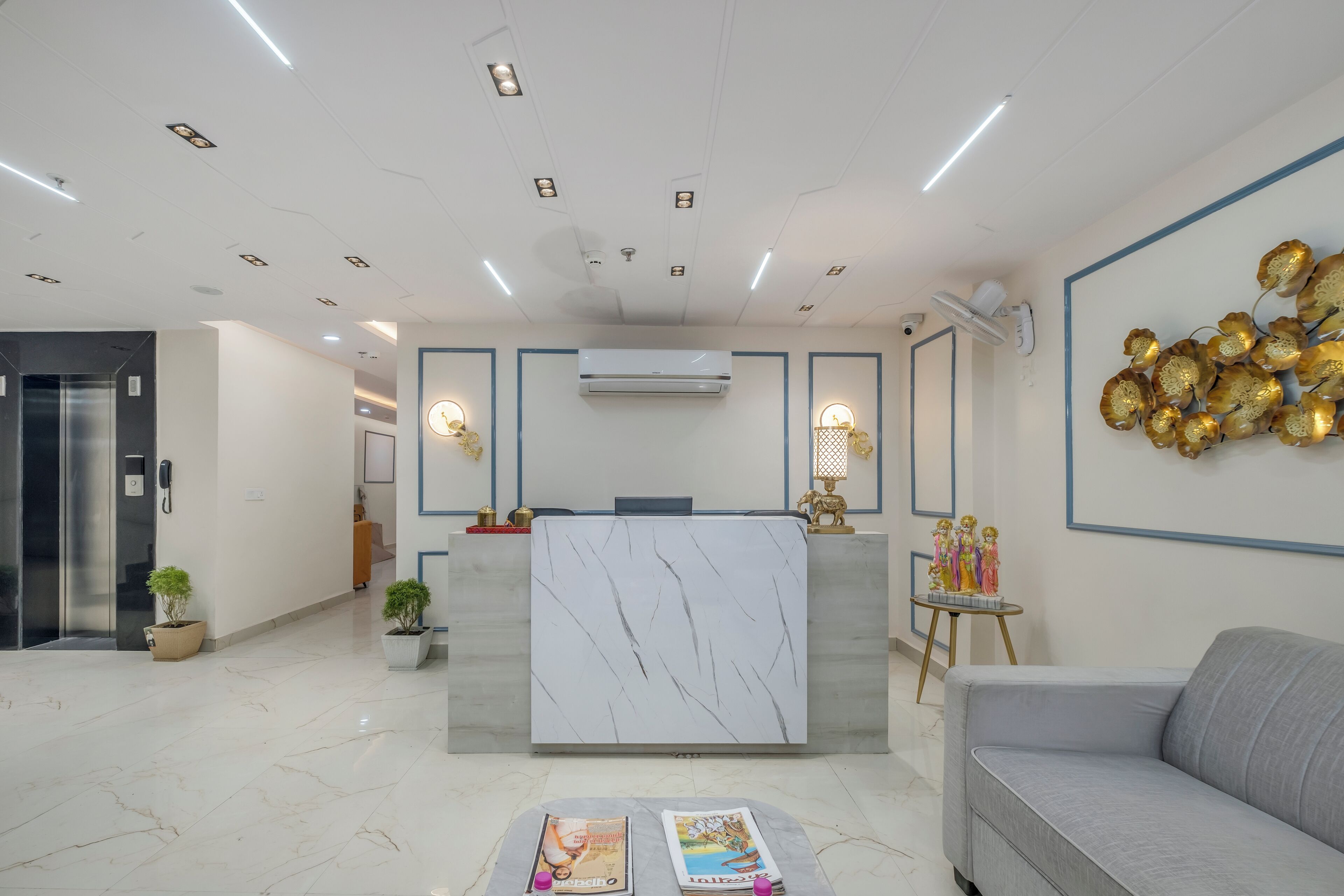 A modern reception area with a marble reception desk, potted plants, a sofa, and a decorative wall piece.