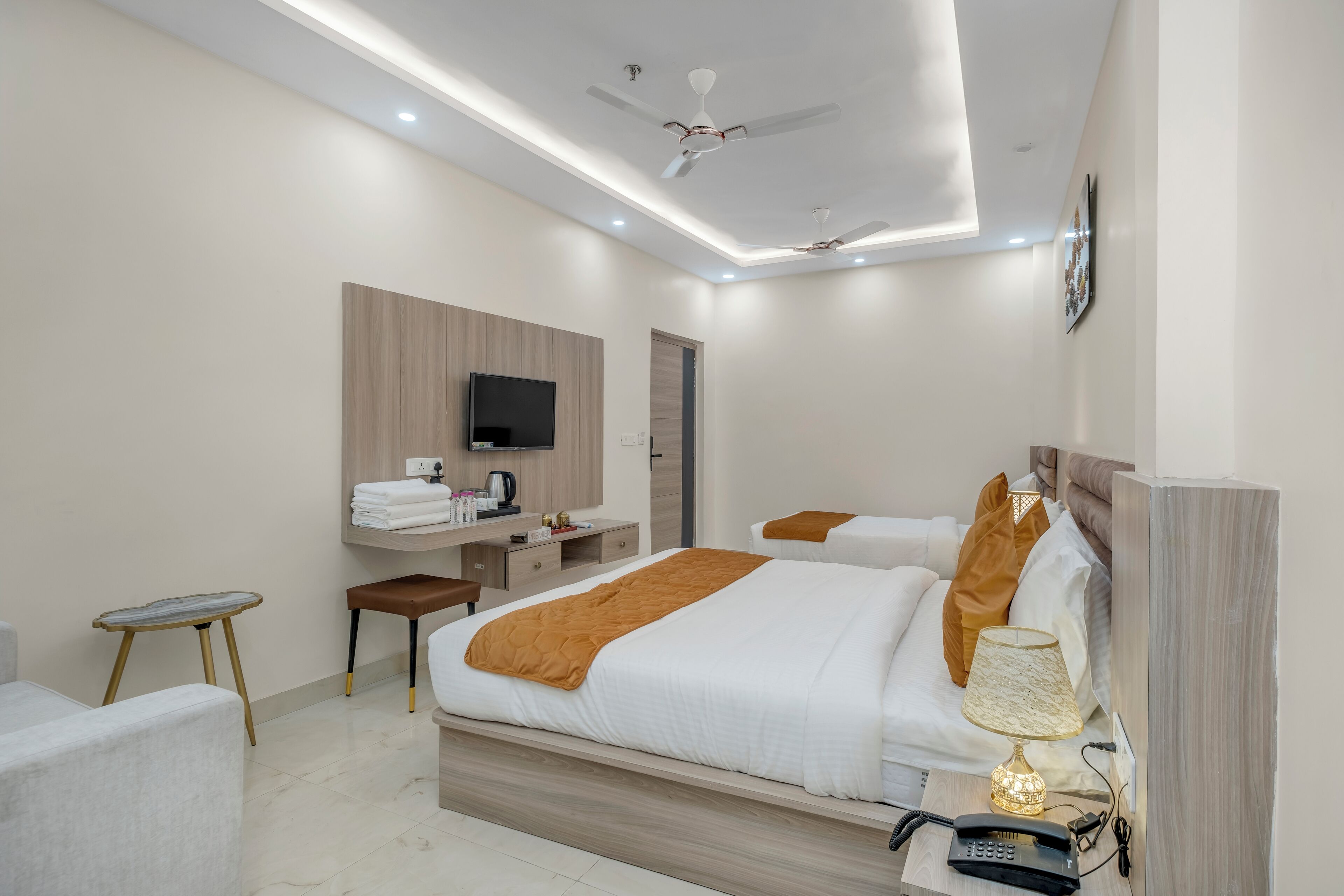 A modern hotel room with a large bed, a desk with a flat-screen TV, a chair, and a bedside table with a lamp.