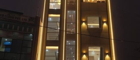 Un hotel llamado "Hotel Sudarshan" con fachada moderna, amplios ventanales y una entrada bien iluminada.