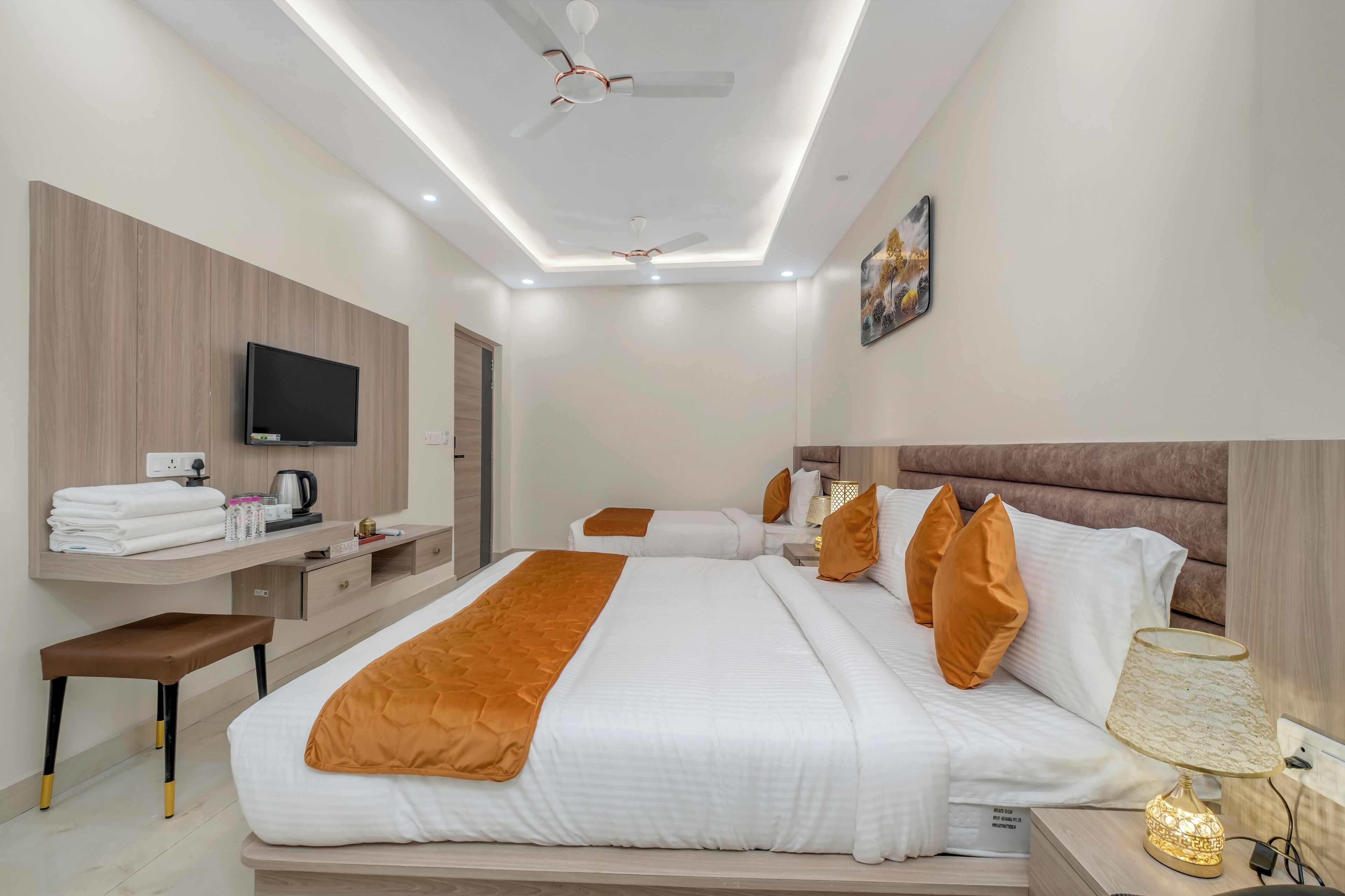 A modern hotel room with a large bed, a TV mounted on the wall, a desk with a kettle, and a ceiling fan.