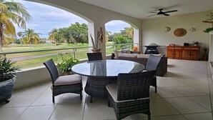 A covered patio with a round table and wicker chairs, overlooking a golf course.