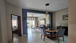 A spacious dining area with a round table and chairs, a ceiling fan, and a view of the outdoors.