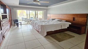 A bedroom with a bed, a chair, a ceiling fan, and a view of the outdoors through a sliding door.