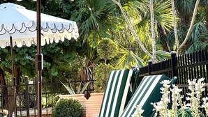 Ein Patio mit weißer Markise, grün gestreiften Liegestühlen und Kübelpflanzen.