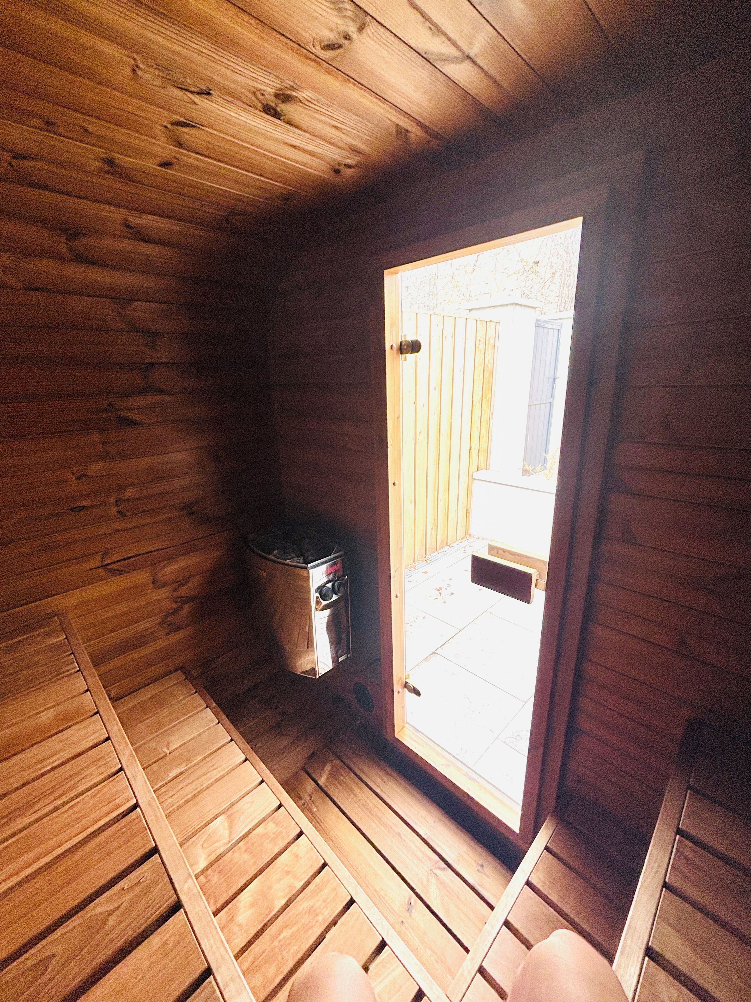 Une cabane en bois avec un petit espace extérieur, une porte donnant sur l’extérieur et un conteneur métallique situé près de la porte.