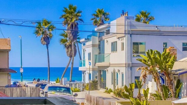 A coastal residential area with modern buildings, palm trees, and a clear view of the ocean. - Coastal Haven (San Diego)