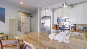 A modern kitchen with white cabinets, stainless steel appliances, and a marble countertop. - Coastal Haven (San Diego)