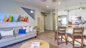 A modern living room with a grey sofa, a coffee table, and a colorful abstract painting on the wall. - Coastal Haven (San Diego)