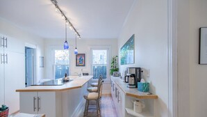 Una cocina moderna con una isla central, armarios blancos y una encimera larga. Hay luces colgantes, una cafetera y un tostador en la isla.