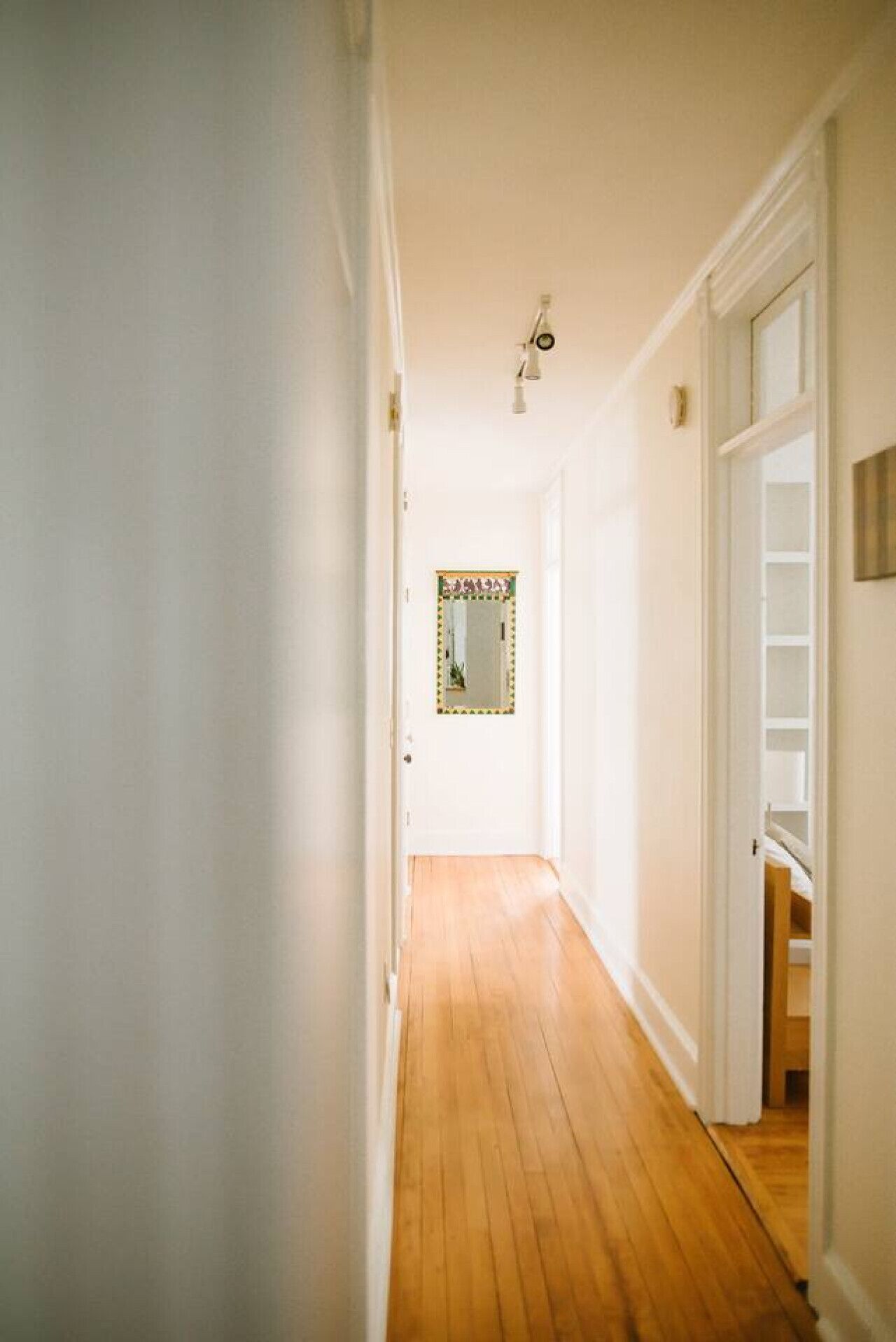 A narrow hallway with wooden flooring and white walls.