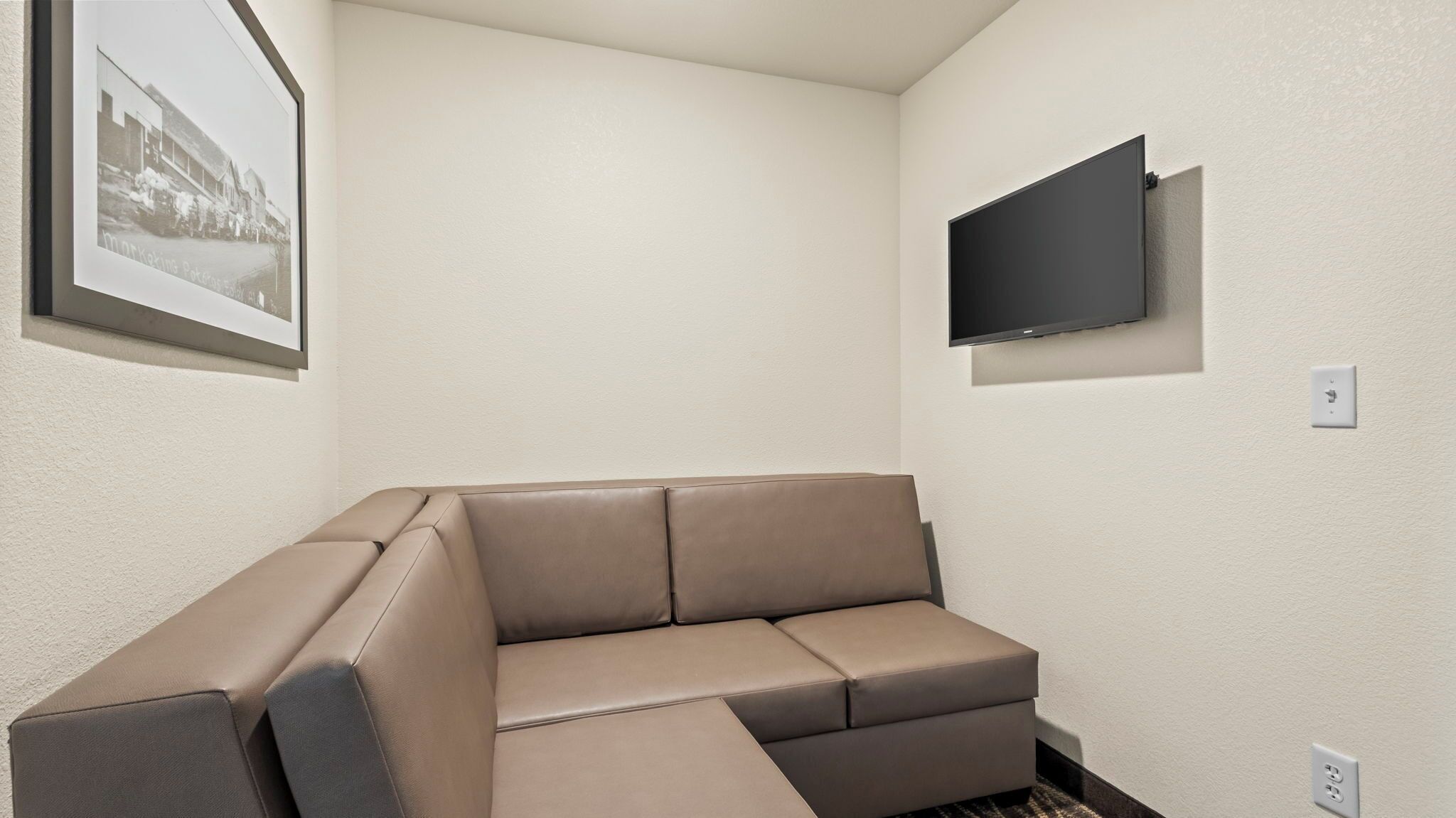 Een hoekappartement met een beige hoekbank, een flatscreen televisie aan de muur en een ingelijst beeld aan de linkerkant.