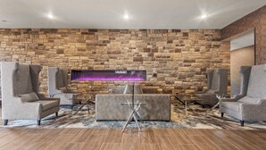 Uma sala de estar moderna com parede de pedra, assentos estofados cinzas e uma mesa de centro de vidro.