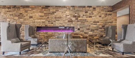 Una sala de estar moderna con pared de piedra, asientos tapizados en gris y una mesa de centro de vidrio.