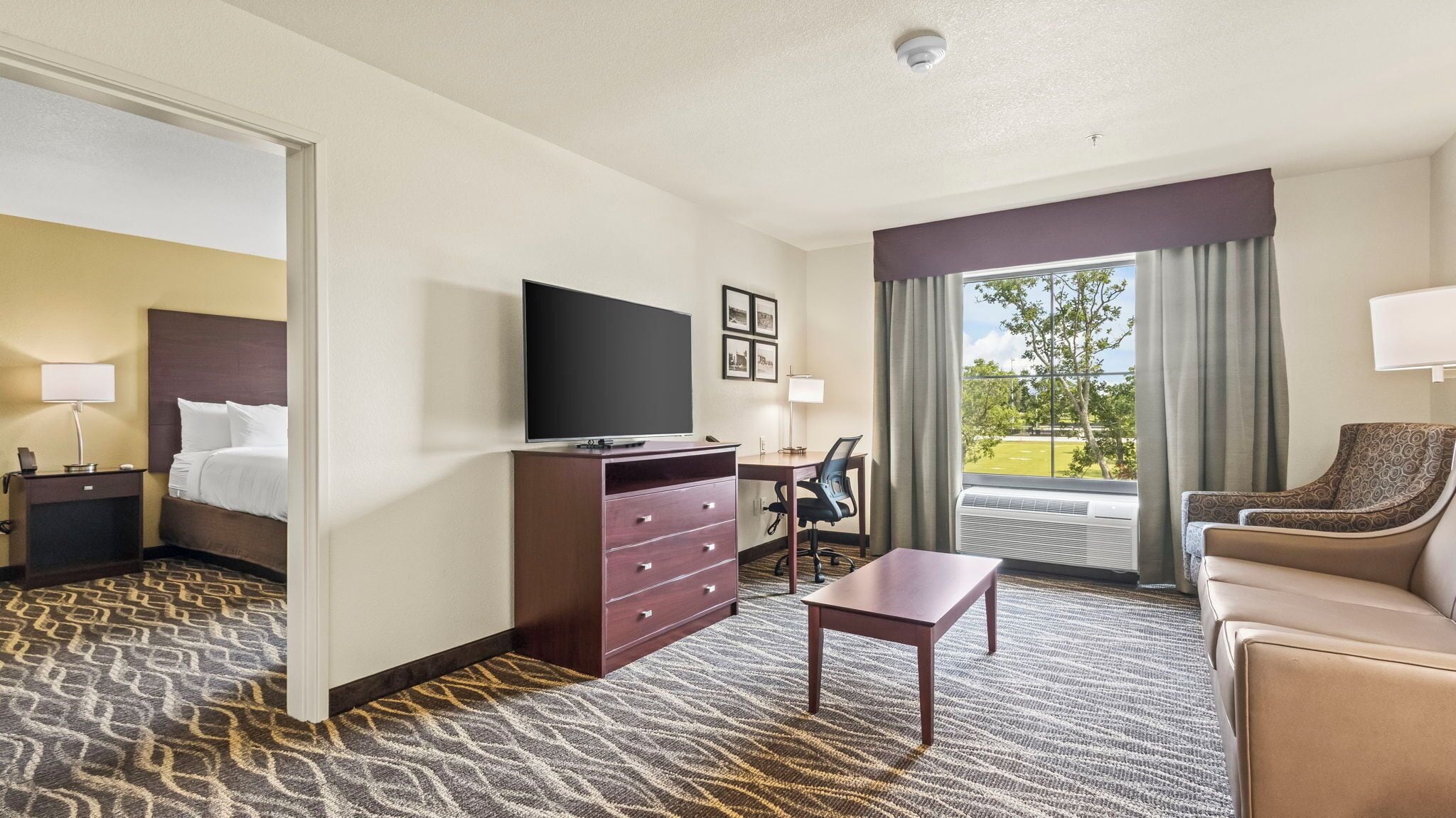 Quarto de hotel com cama, escrivaninha, televisão, cômoda, cadeira e sofá.