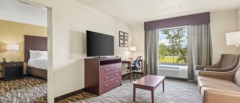 Quarto de hotel com cama, escrivaninha, televisão, cômoda, cadeira e sofá.