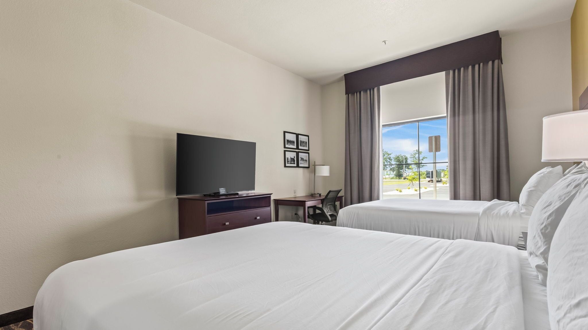 Habitación de hotel con dos camas, un televisor de pantalla plana, un escritorio y un ventanal con cortinas.