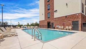 A pool area with lounge chairs and a brick building.