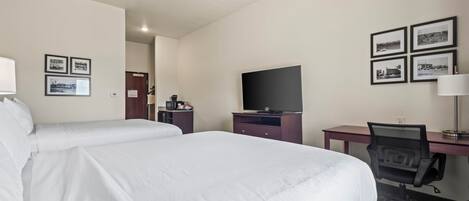 Habitación de hotel con dos camas, un escritorio con computadora, televisor y cuadros en la pared.