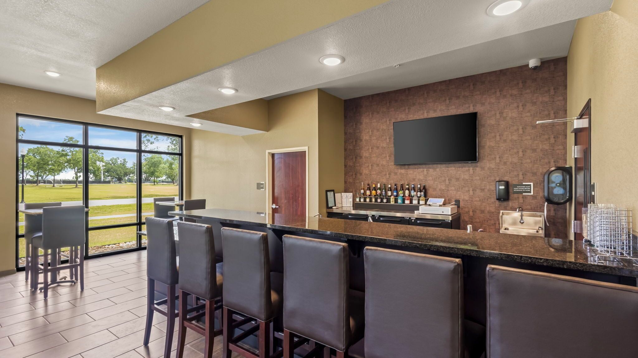 A bar area with a counter, seating, and a large window offering a view of a park.