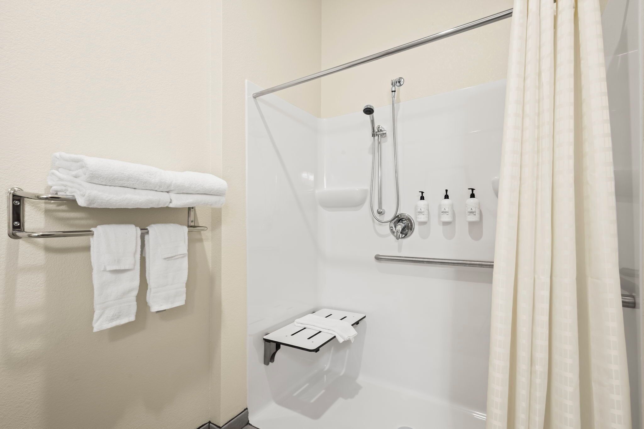 A shower area with a glass door, a towel rack with folded towels, a soap dispenser, and a small shelf.