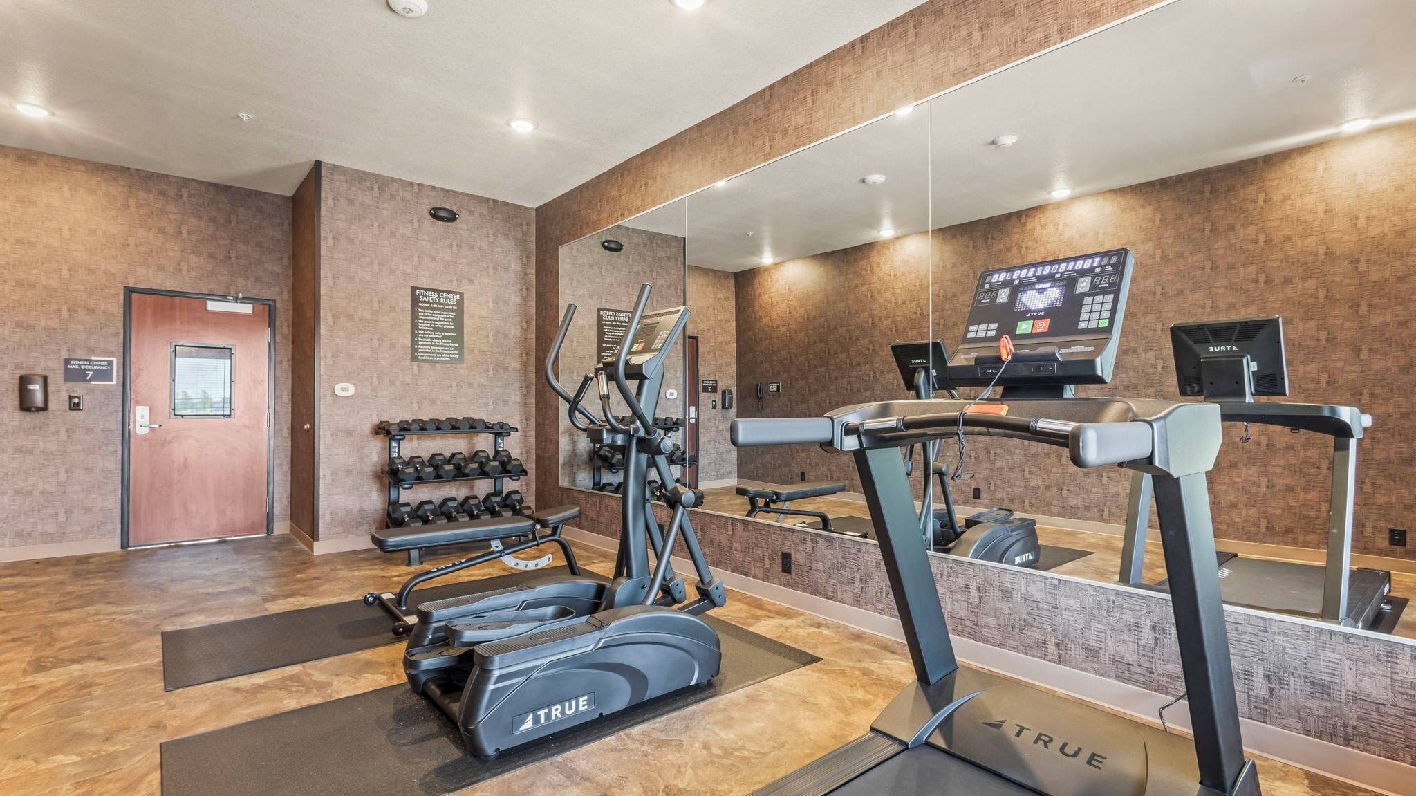 Un gimnasio con cintas de correr, elípticas y un estante de mancuernas.