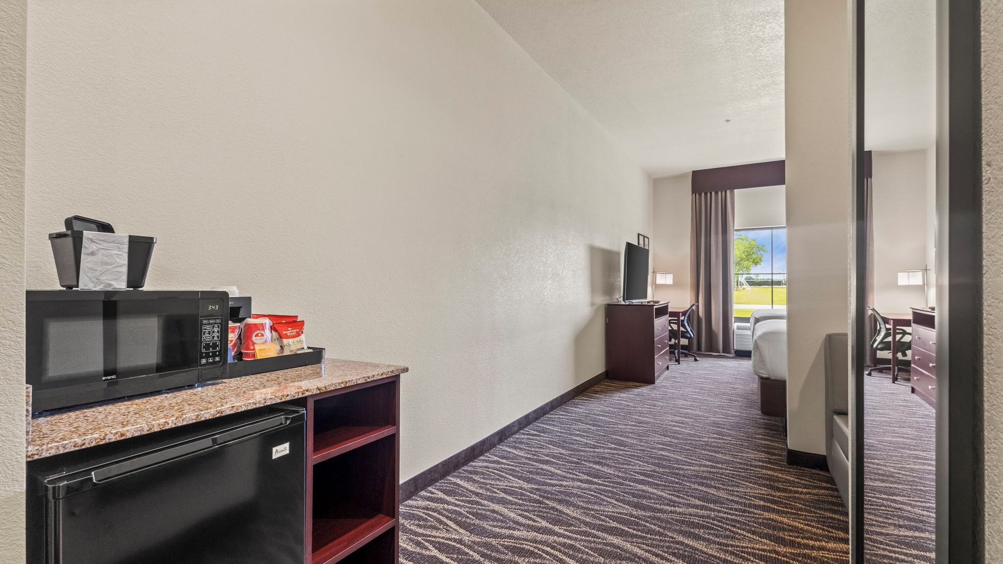 Una habitación de hotel con kitchenette, televisión, escritorio y cama.