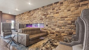 Uma sala de estar moderna com parede de pedra, sofá de couro, mesa de centro de vidro e uma poltrona grande.