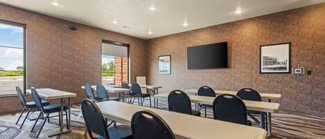 A conference room with tables and chairs, a flat-screen TV, and a window with a view of a road and greenery.