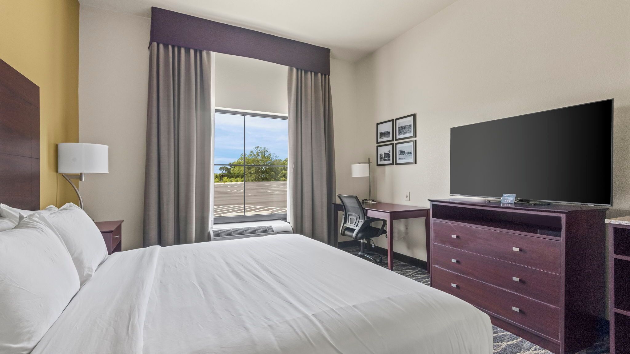 A hotel room with a large bed, a desk with a chair, a television, and a view of the outdoors.