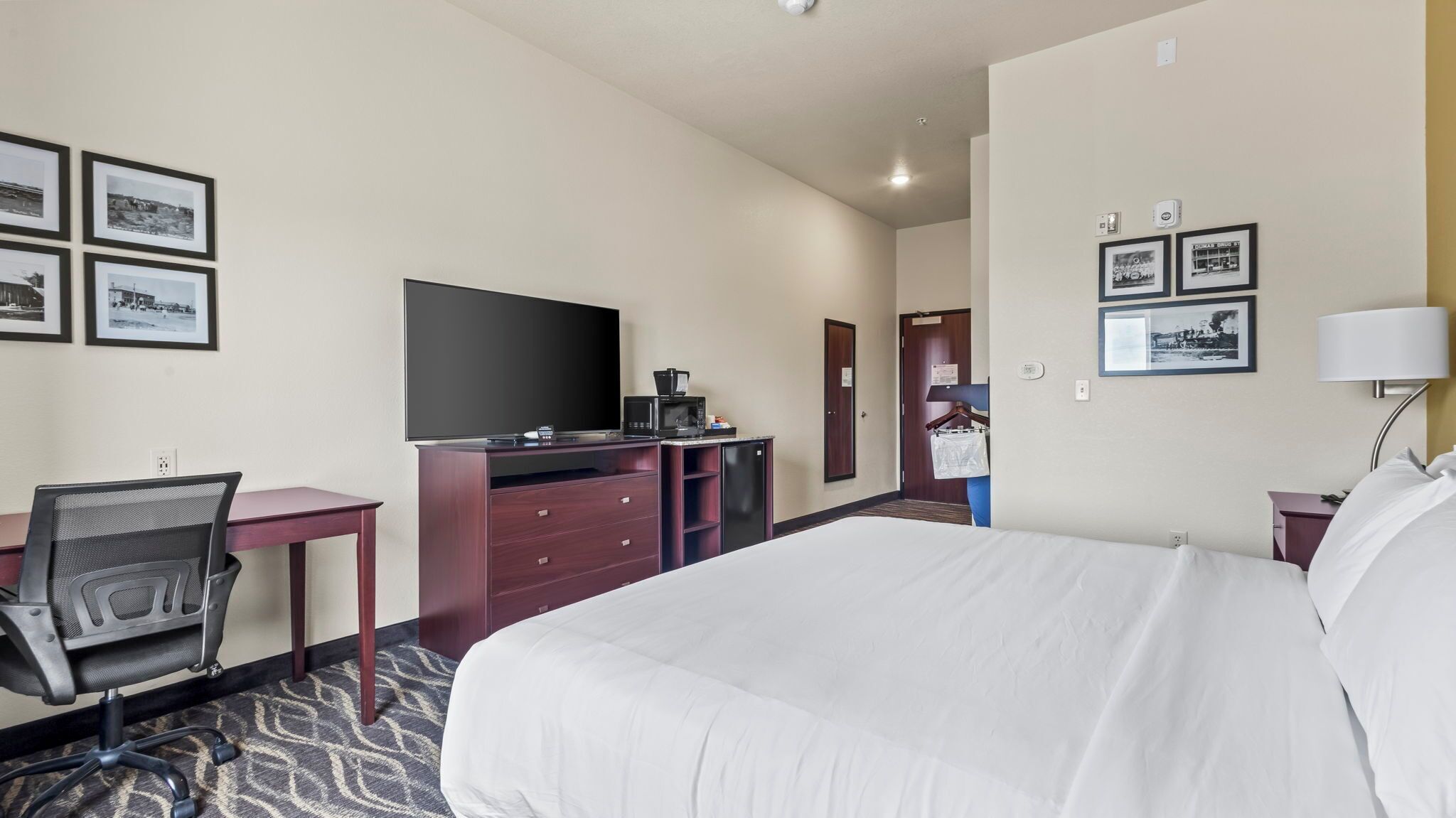 A hotel room with a bed, desk, chair, television, and a minibar.