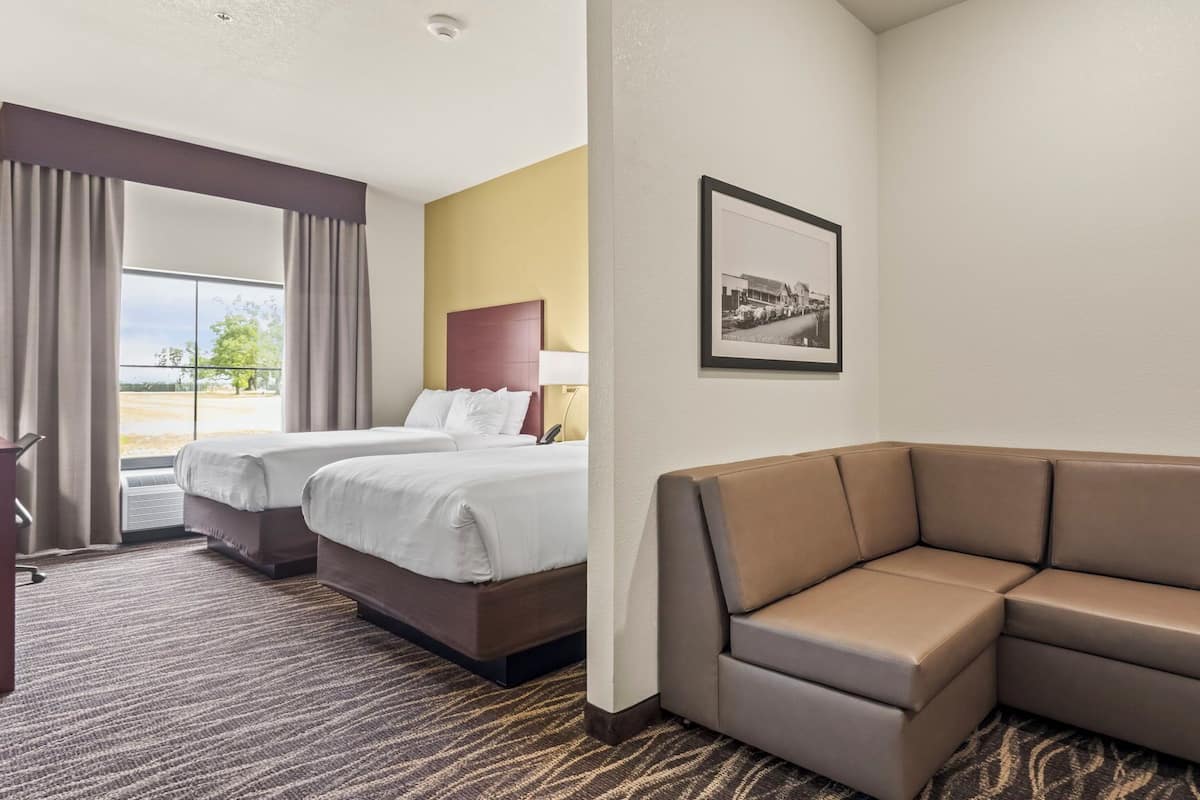 Ett hotellrum med två sängar, en soffa, en inramad tavla på väggen och ett fönster med gardiner.