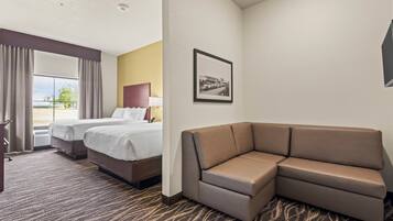 Quarto de hotel com duas camas, um sofá, um quadro pendurado na parede e uma janela com cortinas.