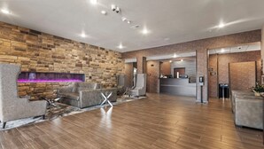 Um hall amplo com parede de pedra, assentos de couro, balcão de recepção e lareira iluminada em roxo.