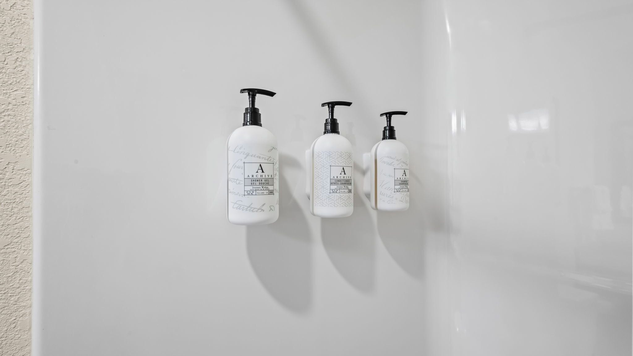 Three white bottles with black pumps on a white wall.