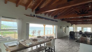 Ein großzügiger Essbereich mit Holztisch und Bänken, großen Fenstern mit Meerblick und einem Fischgrätparkettboden.