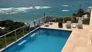 Ein Swimmingpool mit Blick auf das Meer, Liegestühle im Freien und ein Geländer.