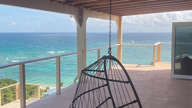 Ein Hängekorbsessel auf einem Balkon mit Blick auf das Meer.
