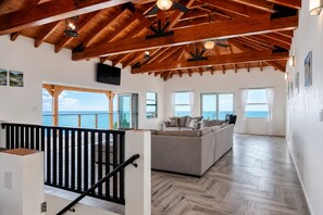 Un amplio salón con techo de madera, un sofá y vista al mar.