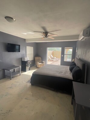 Une chambre à coucher comprenant un lit, un bureau, une chaise, un téléviseur et un ventilateur de plafond.