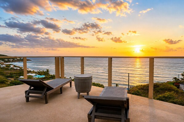 Vista del atardecer desde un balcón con dos sillones de descanso y una mesa redonda.