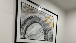 Cama bem arrumada com roupa de cama e almofadas brancas, uma pintura abstrata emoldurada na parede acima e um design de quarto simples e limpo.