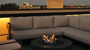 A rooftop seating area with a circular fire pit and a large sofa. - Hotel 1928 (Waco)
