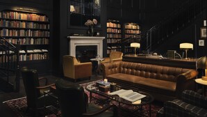 A library with a fireplace, leather sofa, and bookshelves. - Hotel 1928 (Waco)