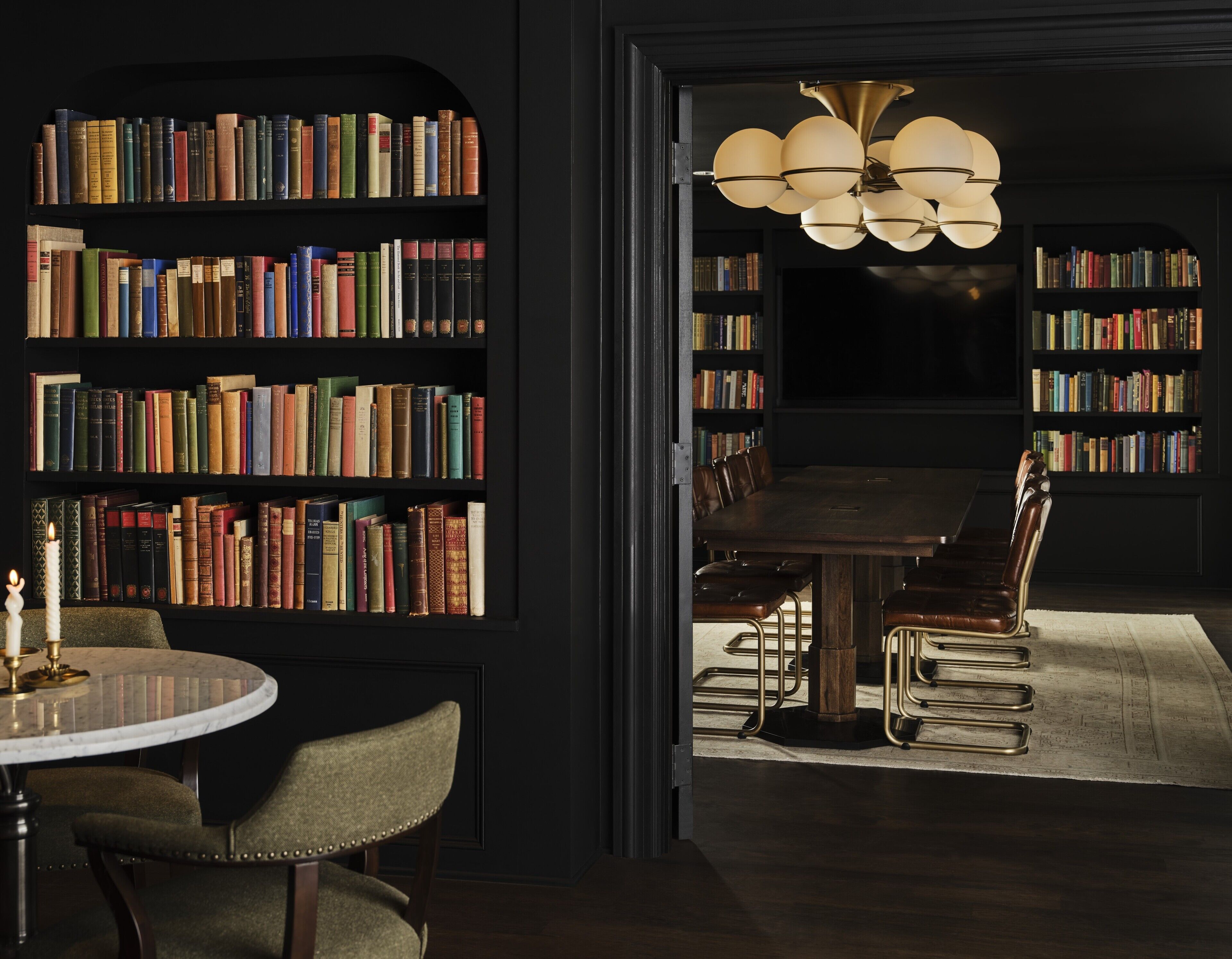 Uma biblioteca com estantes de livros, uma mesa redonda e poltronas de couro.