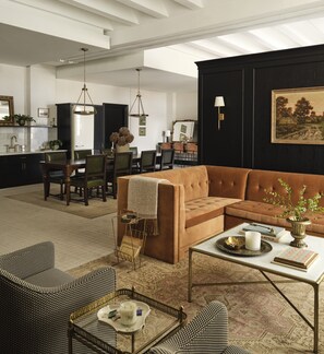 A spacious living room with a brown sofa, a coffee table, and a dining area with chairs and a table. - Hotel 1928 (Waco)