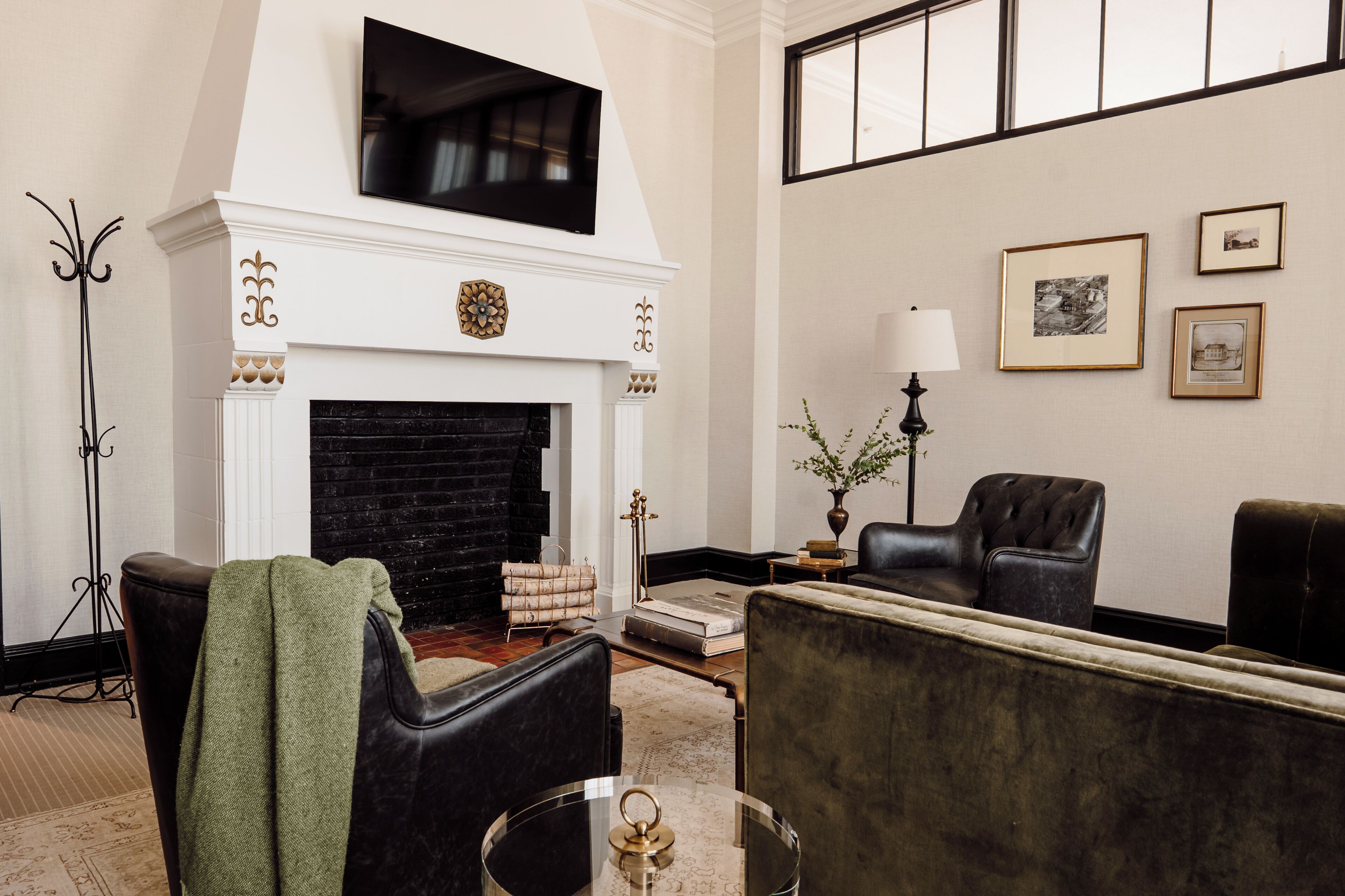 A room with a fireplace, two armchairs, a sofa, a floor lamp, and framed pictures on the wall.
