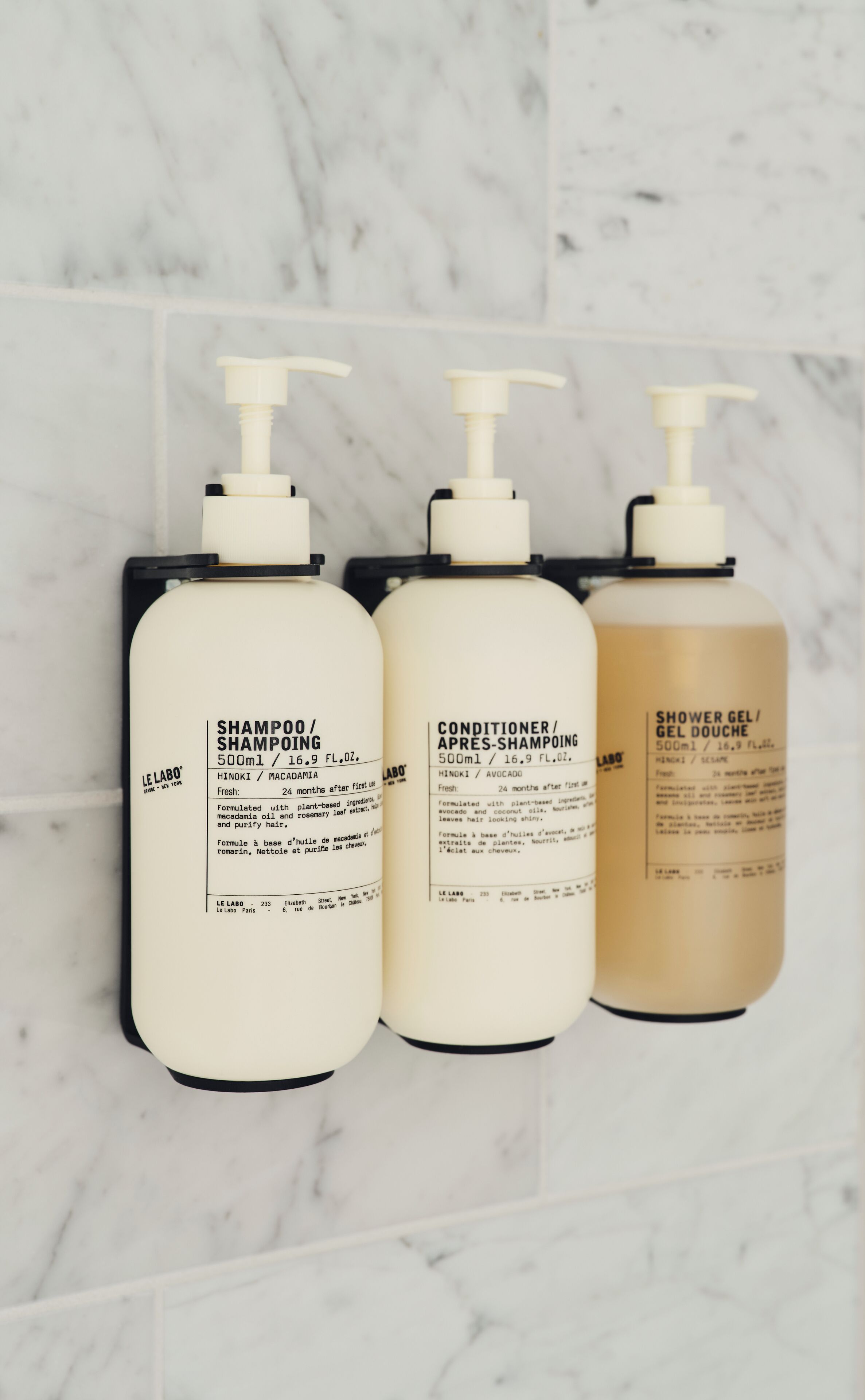 Three Le Labo shampoo bottles on a white marble wall.