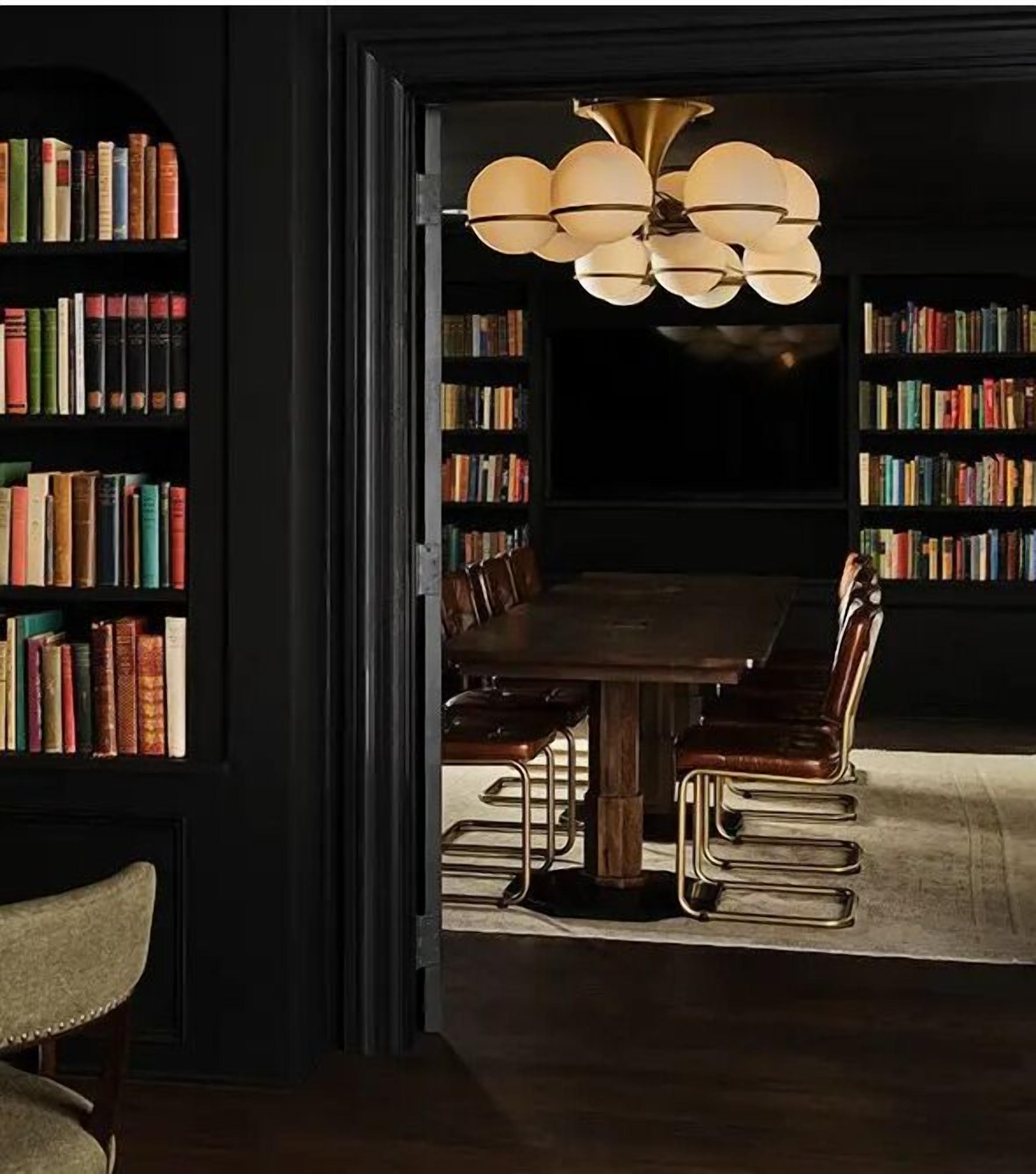 A dining area with a dark wooden table surrounded by leather chairs, a chandelier, and bookshelves filled with books.