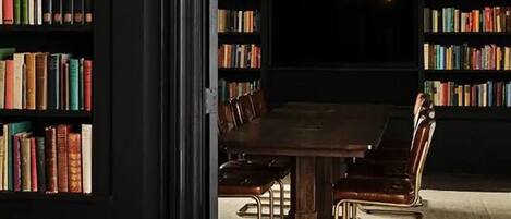 A dining area with a dark wooden table surrounded by leather chairs, a chandelier, and bookshelves filled with books.